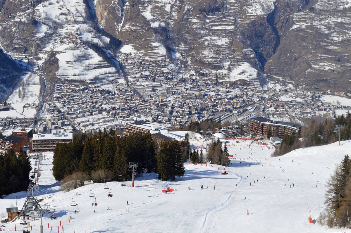 Skiers and chairlifts on a snow-covered piste above Bourg-Saint-Maurice, the town filling the valley floor below under deep winter snow