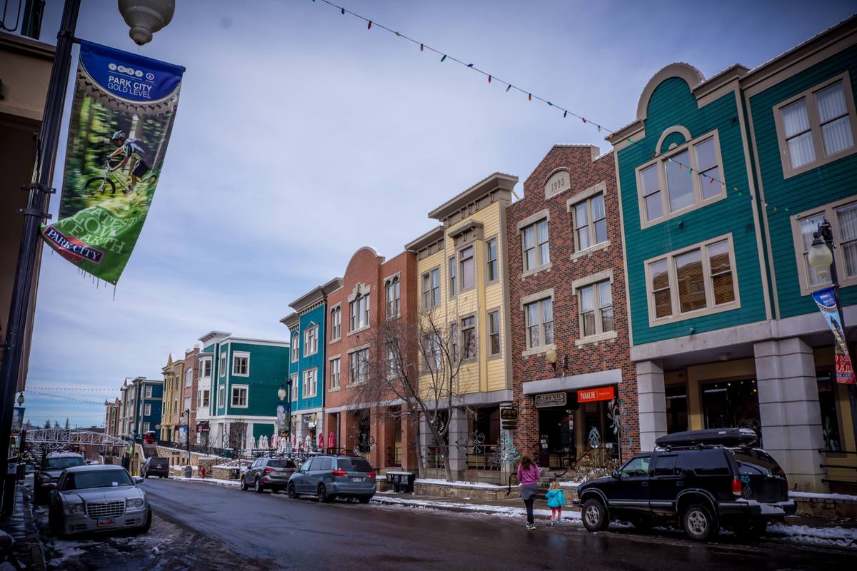 Colorful brick and clapboard storefronts along a snowy Main Street in Park City, with string lights overhead and a Park City banner in the foreground