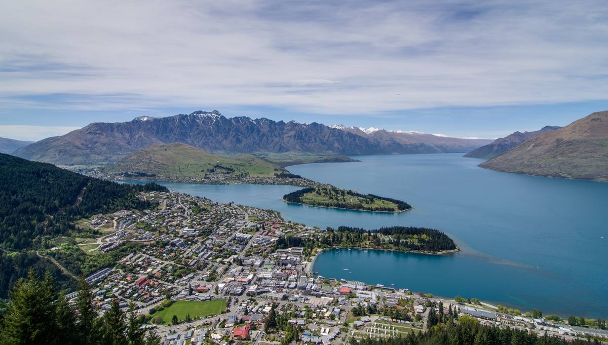 Queenstown's lakefront town curving around turquoise Lake Wakatipu, with light snow on the Remarkables range behind it