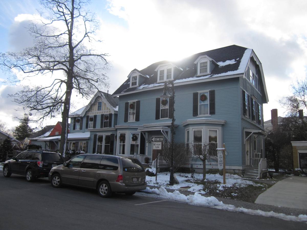 A plowed village street in Lenox on a bright winter day, clapboard houses with holiday wreaths in their windows behind banks of snow and a cast-iron street lamp