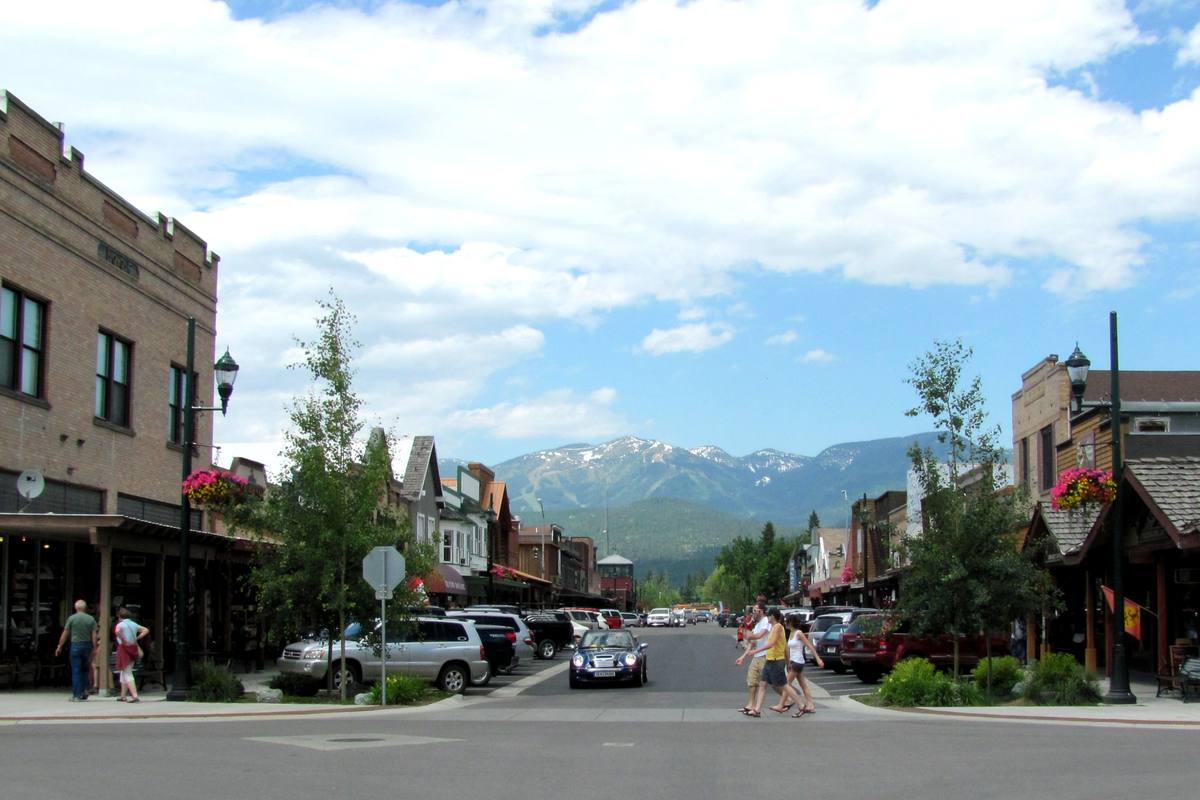 Central Avenue in downtown Whitefish with shopfronts, hanging flower baskets and pedestrians, and the ski runs of Big Mountain rising directly at the end of the street
